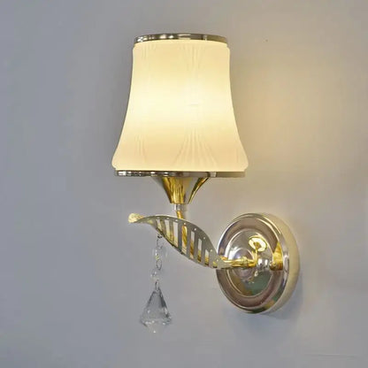 Modern gold bedside wall sconce with a cream textured lampshade and a dangling crystal teardrop for bedroom lighting