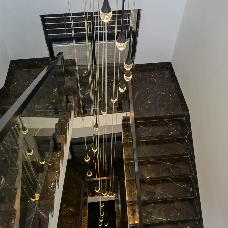 Modern gold crystal bubble chandelier hanging above black marble staircase with glass railings decorbites crystal bubble
