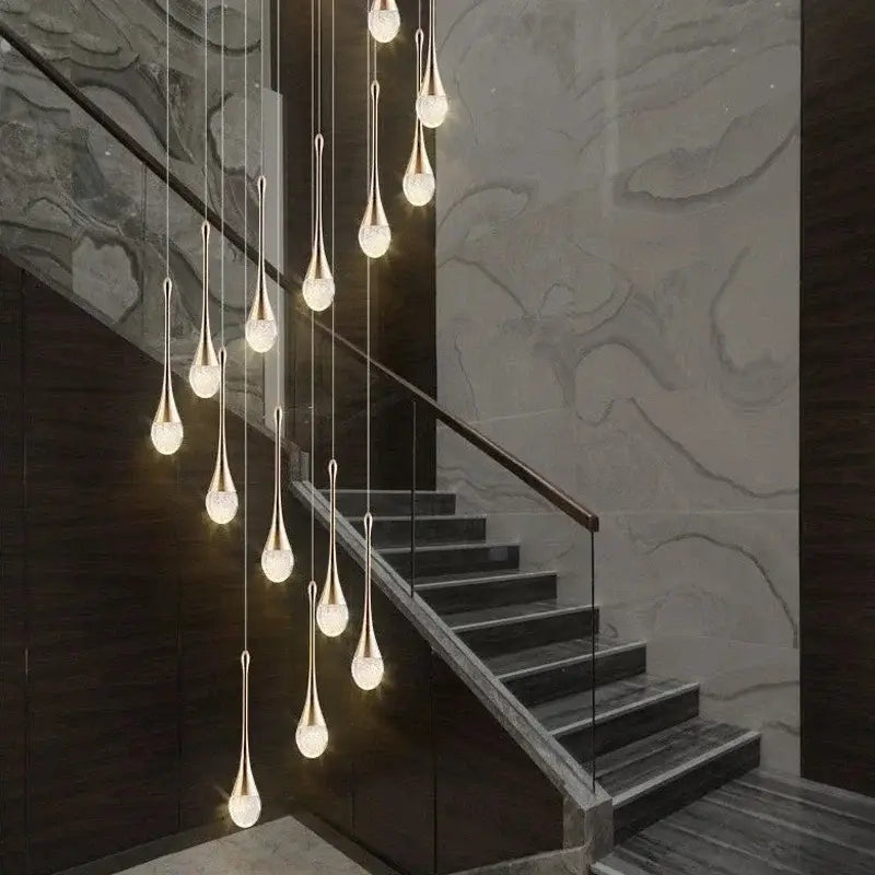 A modern gold decorbites crystal bubble chandelier with teardrop glass shades hangs above a staircase