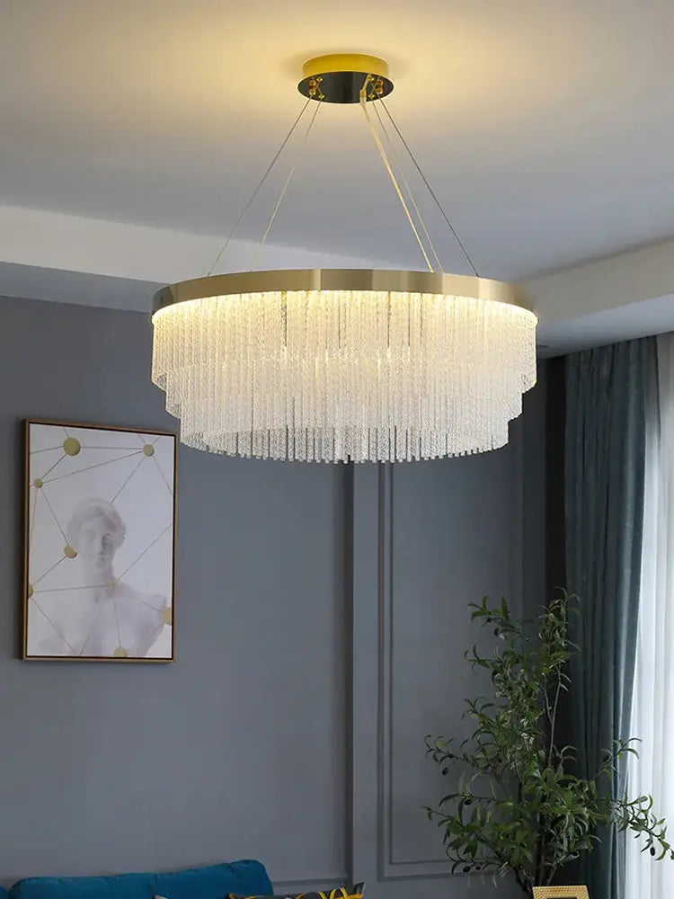 A modern gold crystal ceiling chandelier pendant light with a circular metal frame and cascading clear crystal strands