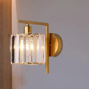 Modern gold wall sconce with cylindrical crystal glass shade featuring vertical facets ideal for bedroom light