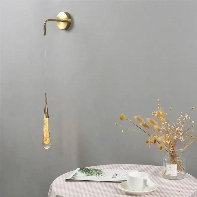 Modern gold crystal droplet wall lamp with a teardrop glass pendant filled with glowing amber liquid decorbites crystal droplet