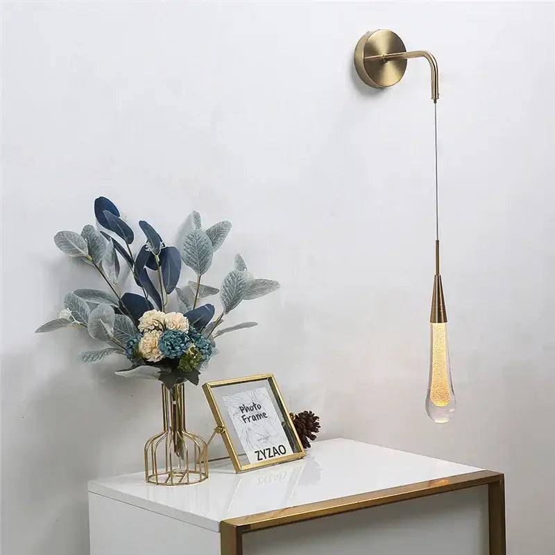 Modern gold crystal droplet wall lamp with slender curved arm and glass pendant filled with glowing golden beads decorbites crystal droplet