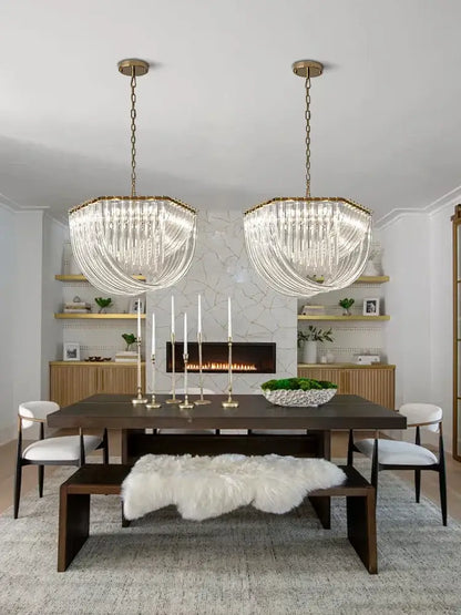 Two elegant modern gold decorbites crystal glass pendant lights hang symmetrically above a dining table chandelier