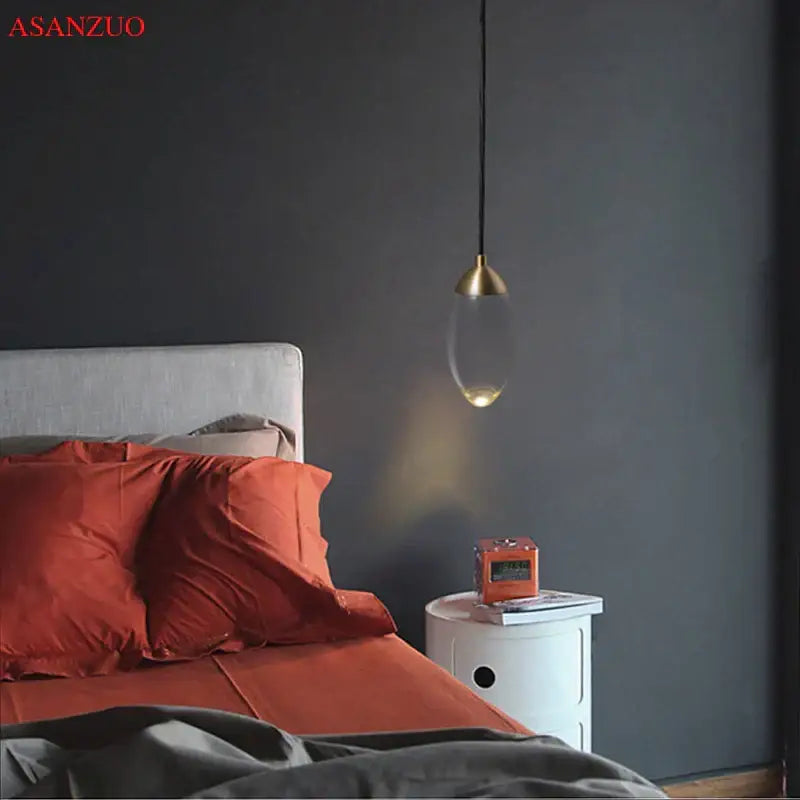 A sleek modern gold crystal led pendant light with a clear glass body hangs from a black cord for bedroom decor