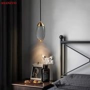 A modern gold crystal led pendant light with a metal frame and glass shade hangs above a bedside table