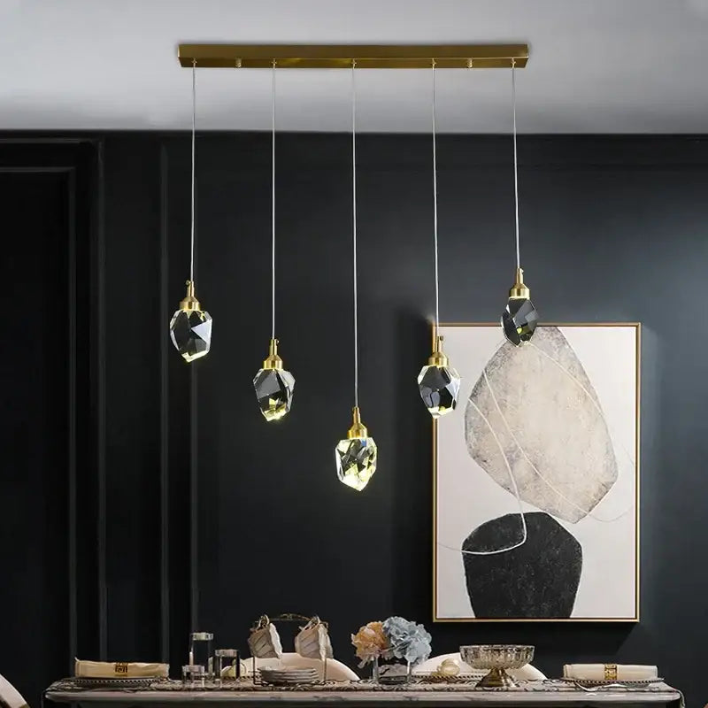 Five faceted crystal led pendant lights with gold-toned metal fixtures hang from a brass bar for dining room