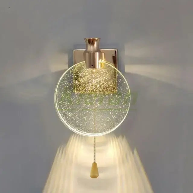 A modern gold crystal led wall lamp with clear glass globe filled with golden glitter and polished brass fixture