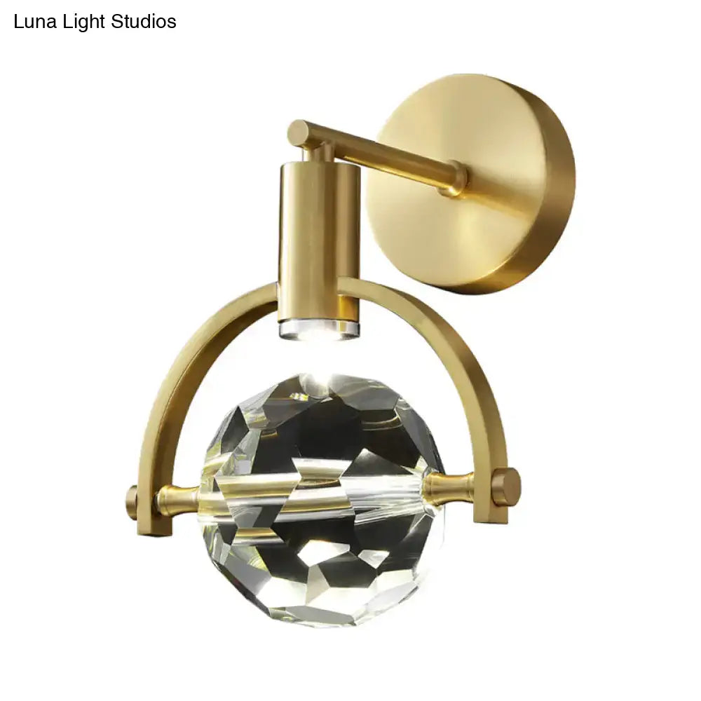 Modern gold led wall lamp featuring a faceted crystal globe with a bulb base suspended by an arched brass frame