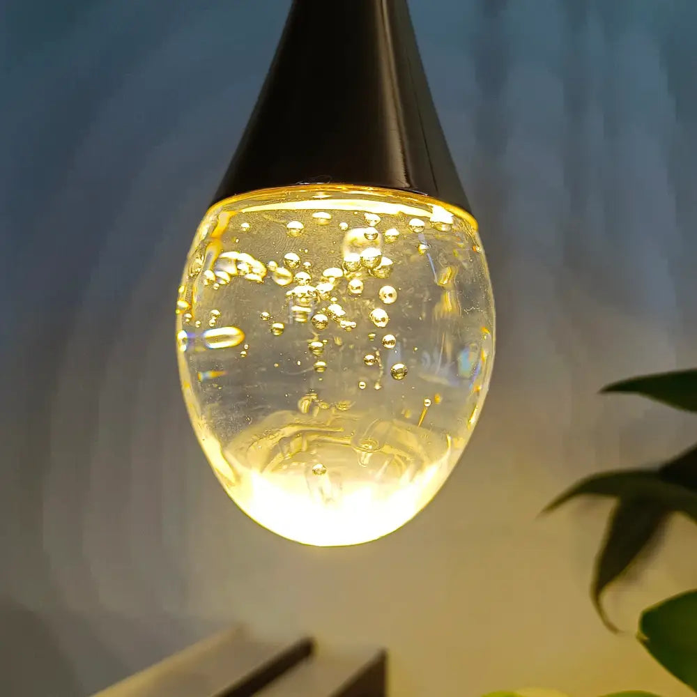 A sleek black-topped modern gold crystal led wall lamp with a teardrop glass globe and glowing golden liquid bubbles