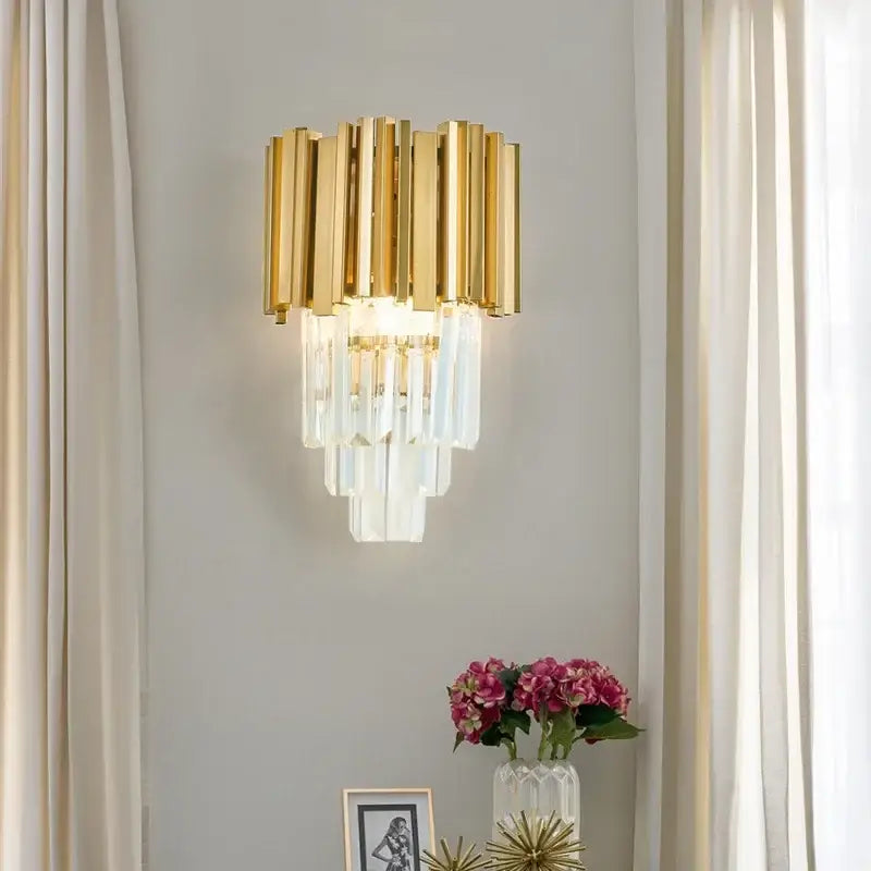 Modern gold crystal led wall lamp with vertical crystal prisms designed as a cascading bedroom sconce light