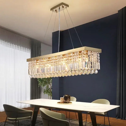 A modern gold crystal pendant light with a rectangular metal frame and cascading clear crystal prisms for dining room