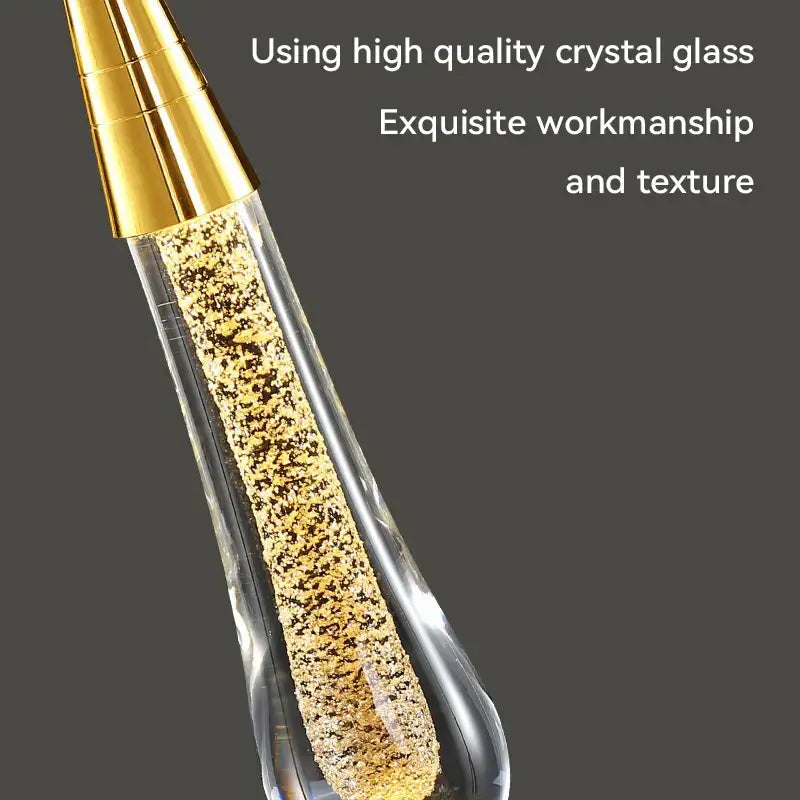 A modern crystal raindrop pendant light with a teardrop shape filled with sparkling gold flakes and a golden cap