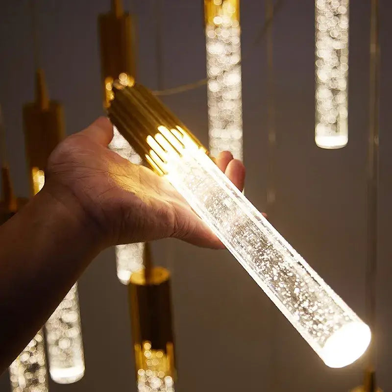 A hand holds a modern gold crystal rotating staircase chandelier with clear acrylic body and warm white light beads
