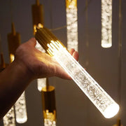 A hand holds a modern gold crystal rotating staircase chandelier with clear acrylic body and warm white light beads
