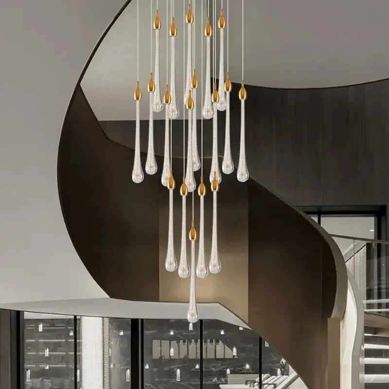 A modern gold crystal rotating staircase chandelier with clear glass teardrop pendants and gold-toned caps