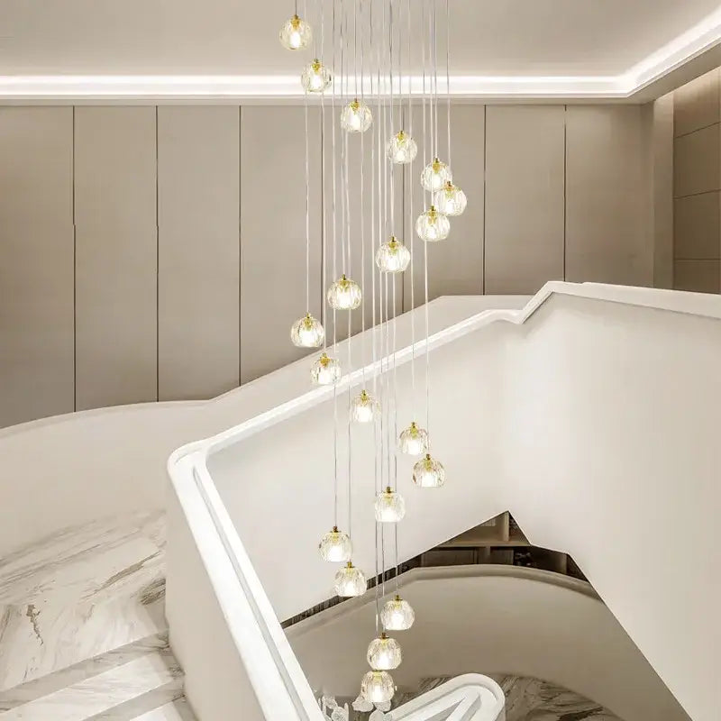 A modern gold crystal stair football shaped chandelier with clear glass globe lights suspended by metallic cords