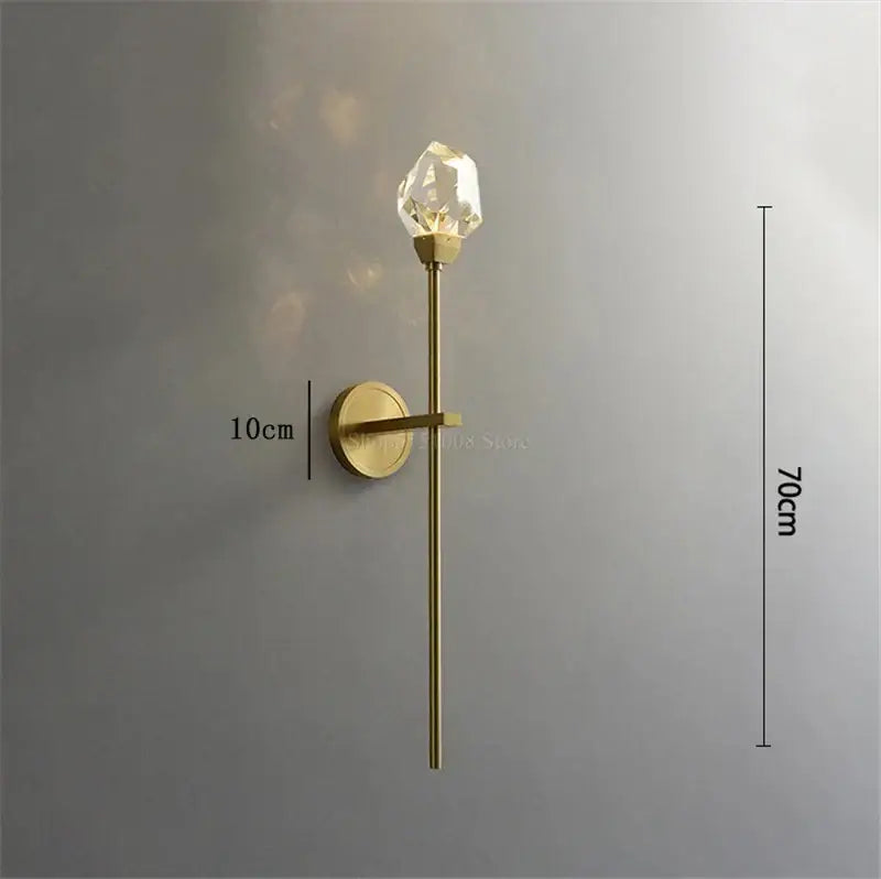 A modern gold crystal wall lamp with a slender stem and faceted crystal bulb for elegant bedroom decorbites crystal wall lighting
