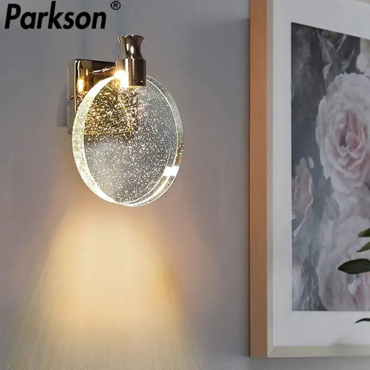 Modern gold crystal wall lamp with a gold-toned parkson wall sconce and clear glass shade featuring sparkling particles
