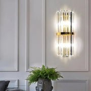 Modern gold crystal wall sconce with vertical rods and metal accents emitting warm glow for 110v-120v living space