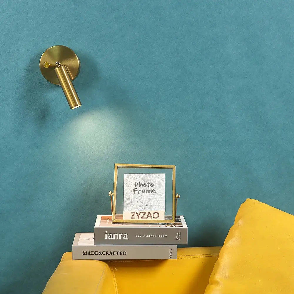 Gold-framed photo frame with clear glass and brass hinges resting on books alongside modern gold led wall lamp decorbites led wall
