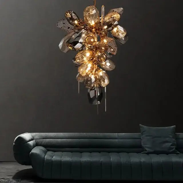 A modern gold decorbites crystal duplex chandelier with faceted amber and clear crystals above a dark teal sofa