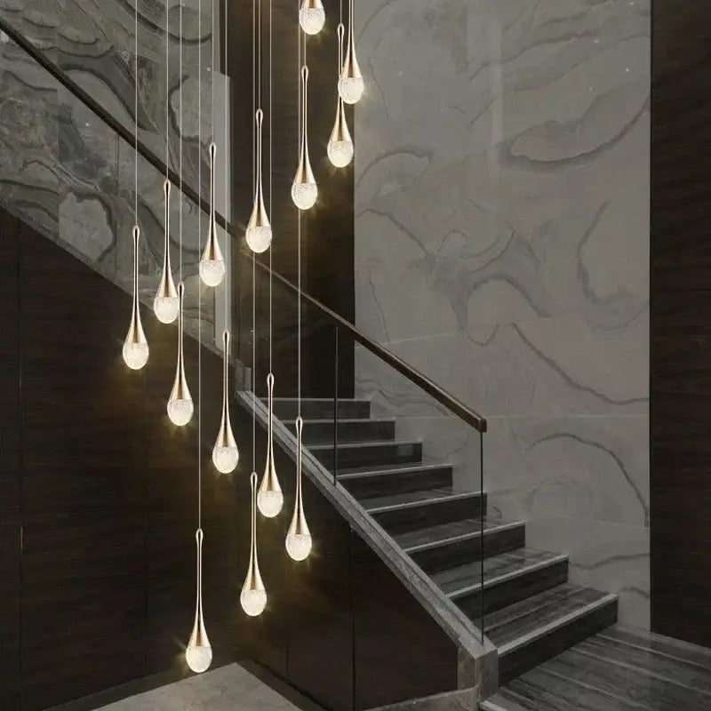 A modern gold-toned decorbites crystal led pendant chandelier with teardrop glass shades hanging above a staircase