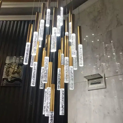A modern gold decorbites crystal staircase chandelier with cylindrical glass tubes filled with sparkling crystals