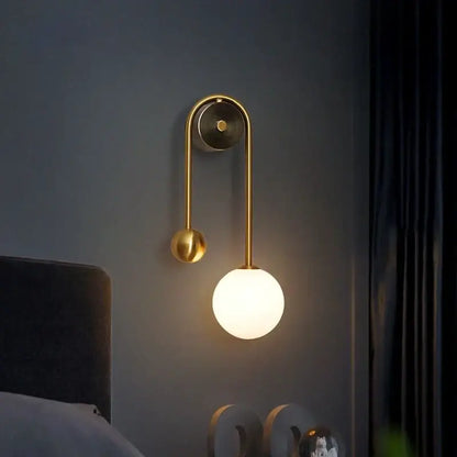 Modern gold decorbites glass ball led wall lamp with a gold-toned curved arm and spherical glass ball shade for bedroom use