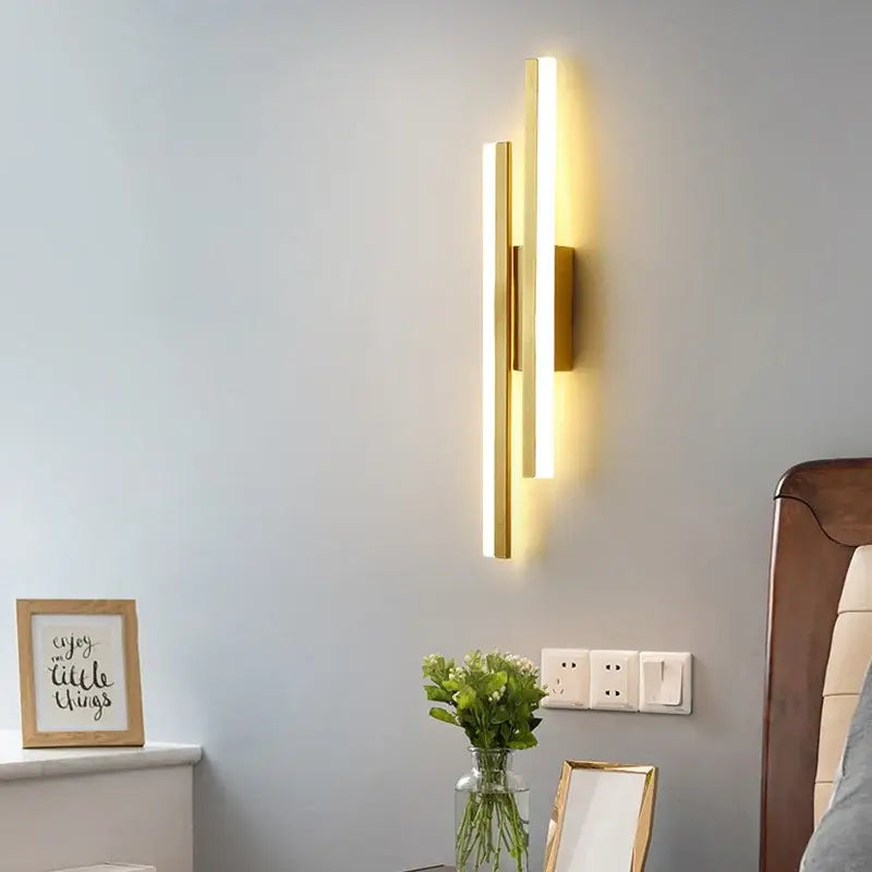 Modern gold-toned decorbites led strip wall lamp with two vertical led bars emitting warm light for bedroom sconce lighting