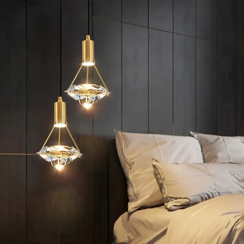 Modern gold diamond crystal pendant lights with crystal shades hanging above a bed for bedroom illumination