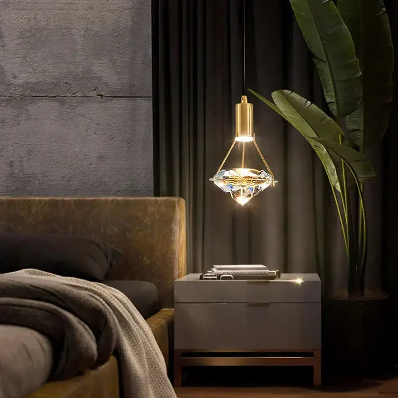 Modern gold diamond crystal pendant light with faceted glass shade emits warm illumination for bedroom lighting