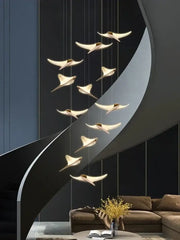 Modern gold-toned decorbites dolphin pendant chandelier lighting a sleek curved hotel lobby staircase setting