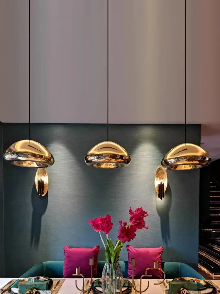 Three sleek golden mushroom-shaped glass gold pendant lamps hanging as dining room decorbites glass gold ceiling lights