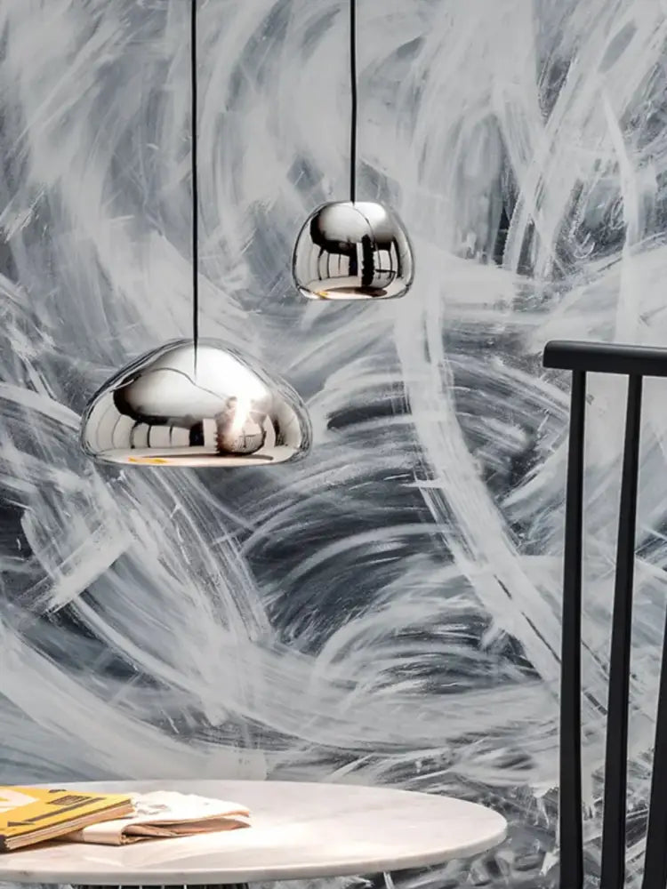 Two sleek chrome pendant lamps with dome design hang on black cords against abstract wall for modern glass gold ceiling decorbites