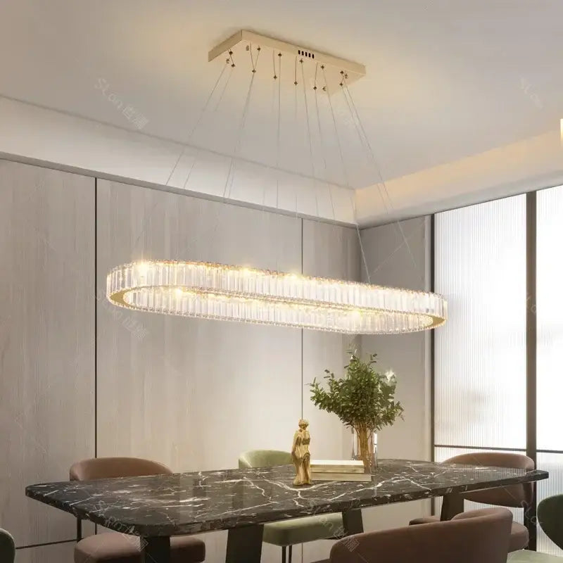 A modern gold decorbites crystal led chandelier with cascading crystal strands above a dark marble dining table