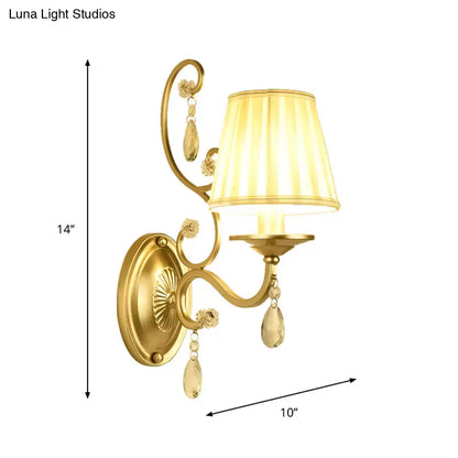 Modern gold fabric wall sconce light fixture with tapered surface, cream pleated shade, and crystal accents for bedroom