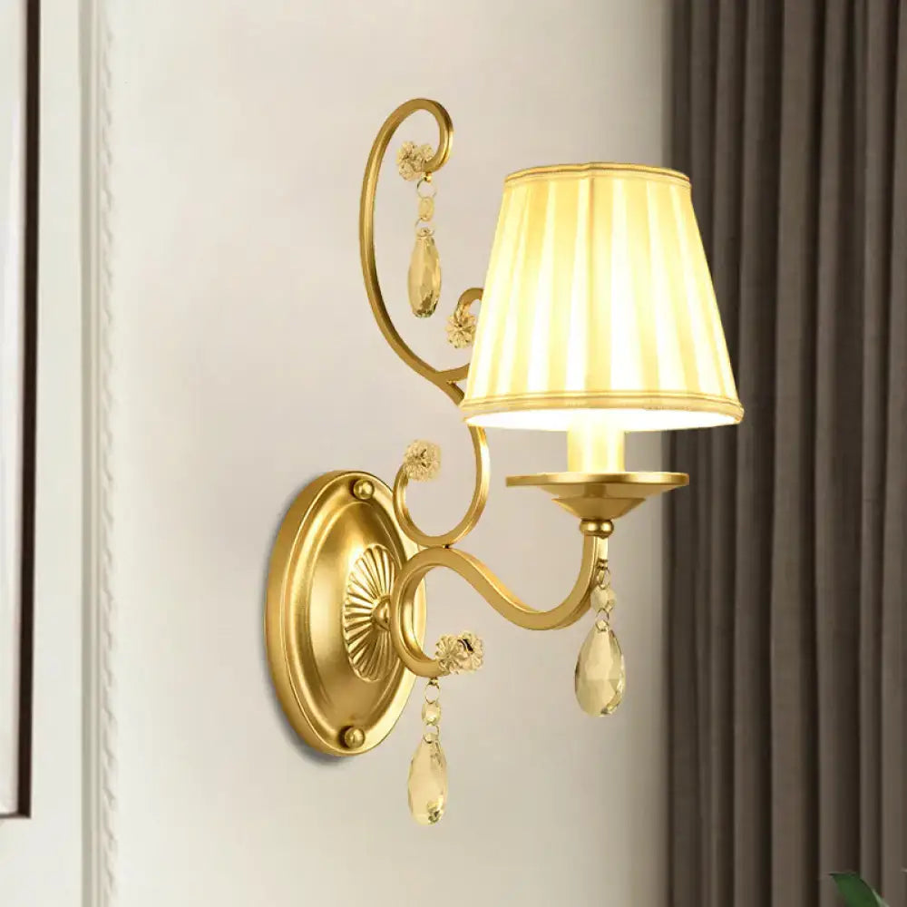 Modern gold fabric wall sconce light fixture with tapered surface, pleated cream lampshade, and crystal accents
