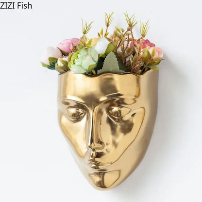 Modern gold decorbites ceramic wall-mounted vase shaped like a stylized human face filled with pink and white flowers
