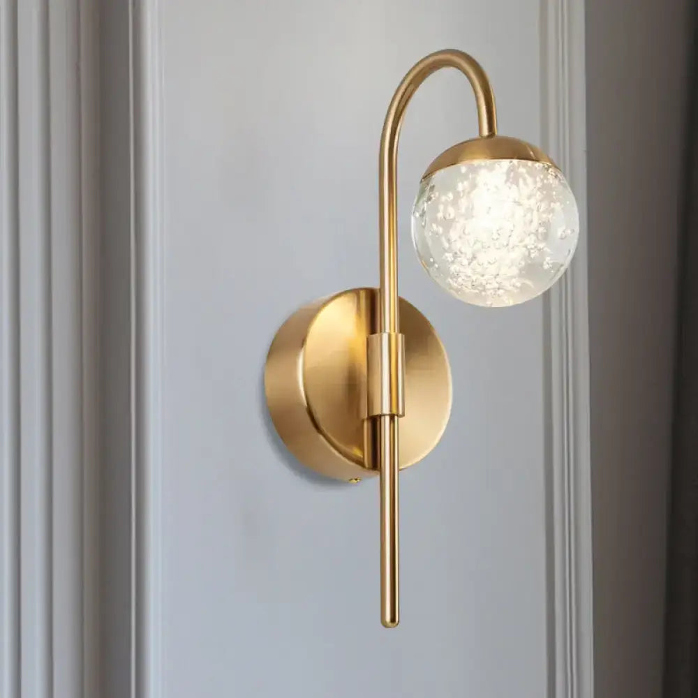 Modern gold finish wall sconce with curved arm and frosted crystal globe for living room lighting