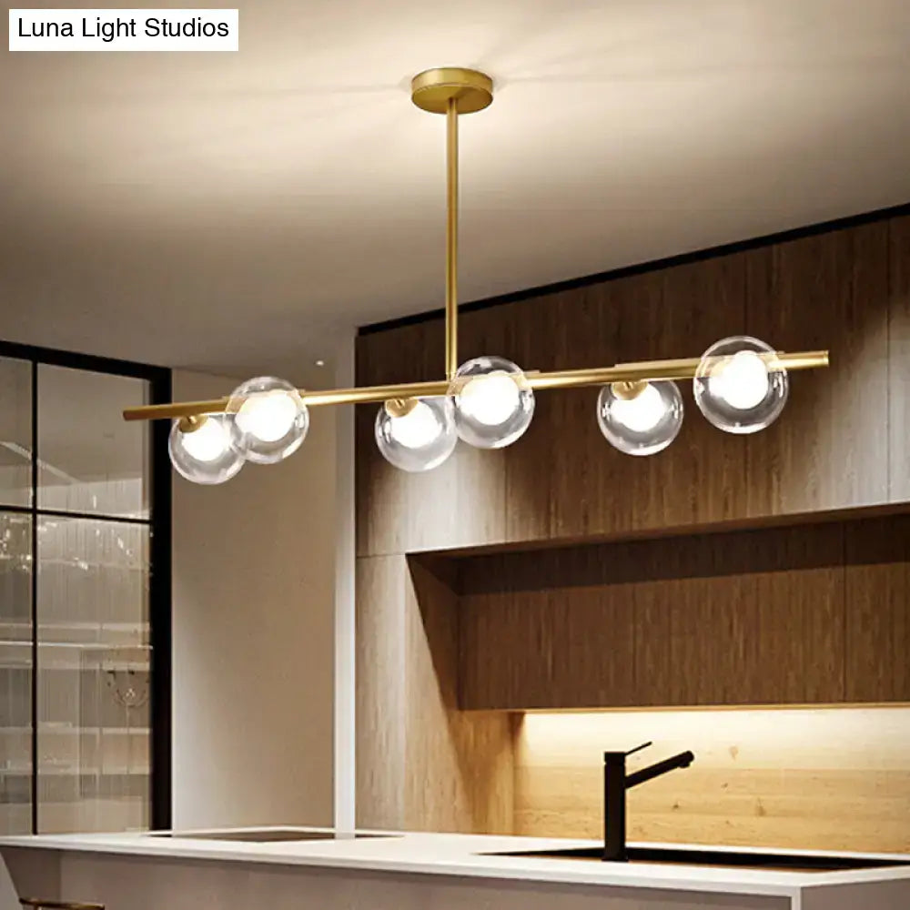 Modern gold finish linear pendant light with five clear glass globe bulbs on a horizontal bar for kitchen use