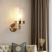 Modern gold finish wall light with clear cylindrical glass shade and adjustable color temperature for bedroom use