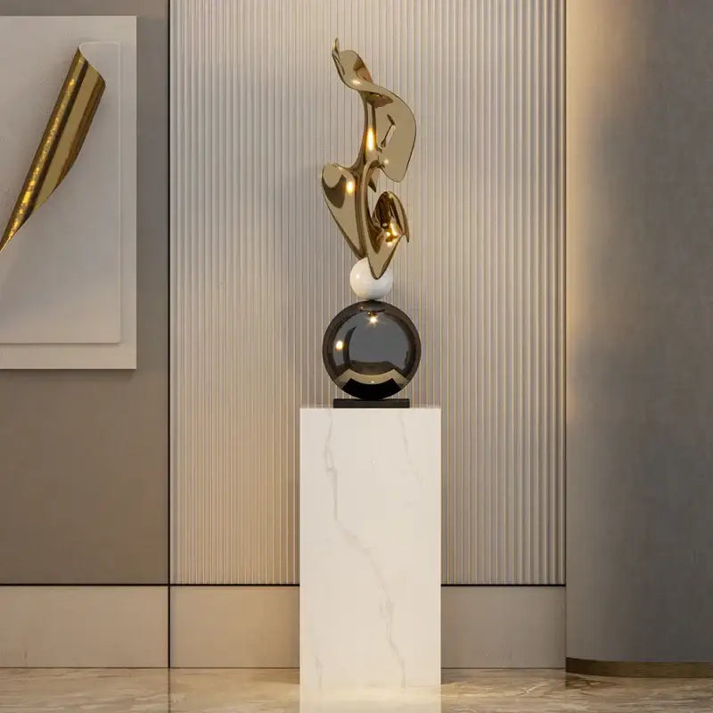 Modern gold geometric electroplating art sculpture with flowing forms on black sphere and white marble pedestal decorbites decor