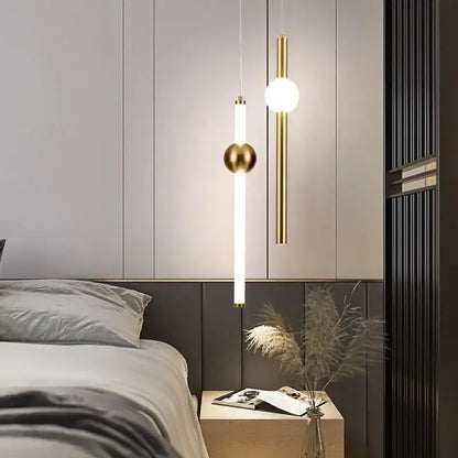 Modern gold geometric line frame pendant lights with cylindrical and spherical glass globes hang above a bedside table