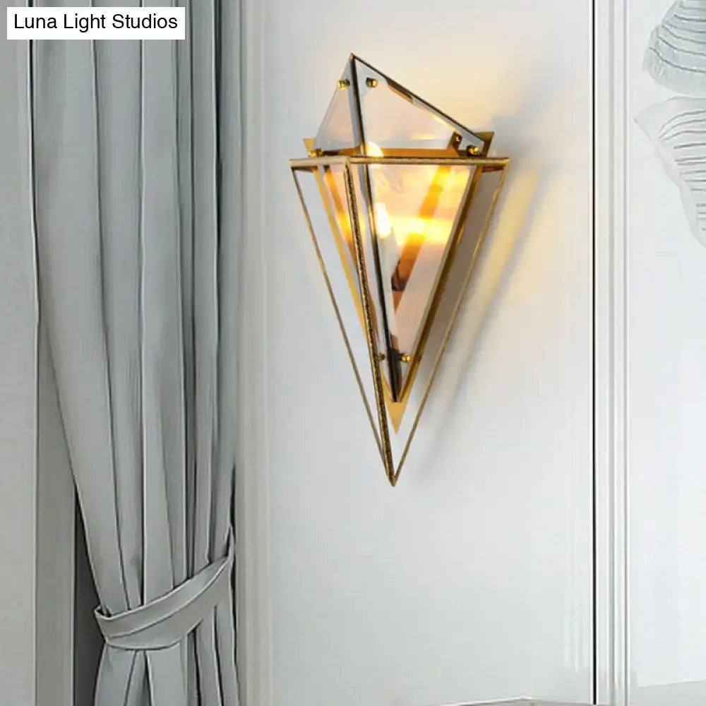 Modern gold geometric wall sconce with clear amber glass panels and warm glowing light for living room use