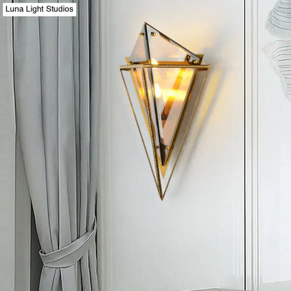 Modern gold geometric wall sconce with clear amber glass panels and warm glowing light for living room use