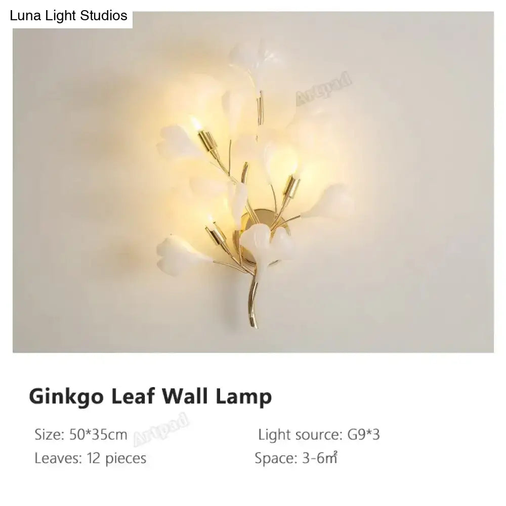 Modern gold ginkgo leaf porcelain wall sconce with delicate white leaf and gold-toned metal branches emitting warm glow