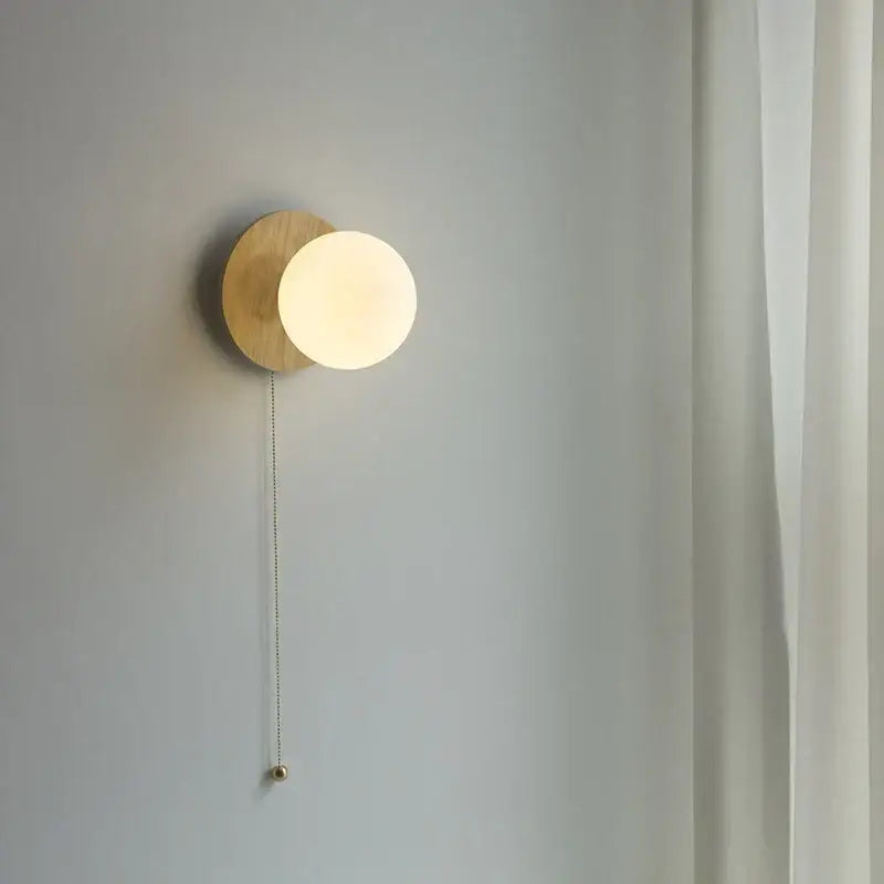 Minimalist wall lights featuring a warm frosted glass ball mounted on a wooden base with a metallic pull chain for bedroom decorbites glass ball