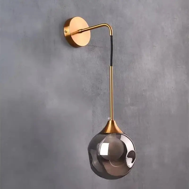 A sleek gold-toned wall sconce with a curved arm and teardrop-shaped smoked glass globe decorbites glass ball gold