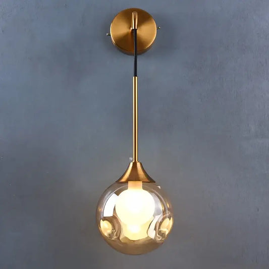 Modern gold wall sconce featuring a sleek glass ball teardrop lamp with an illuminated bulb by decorbites glass ball